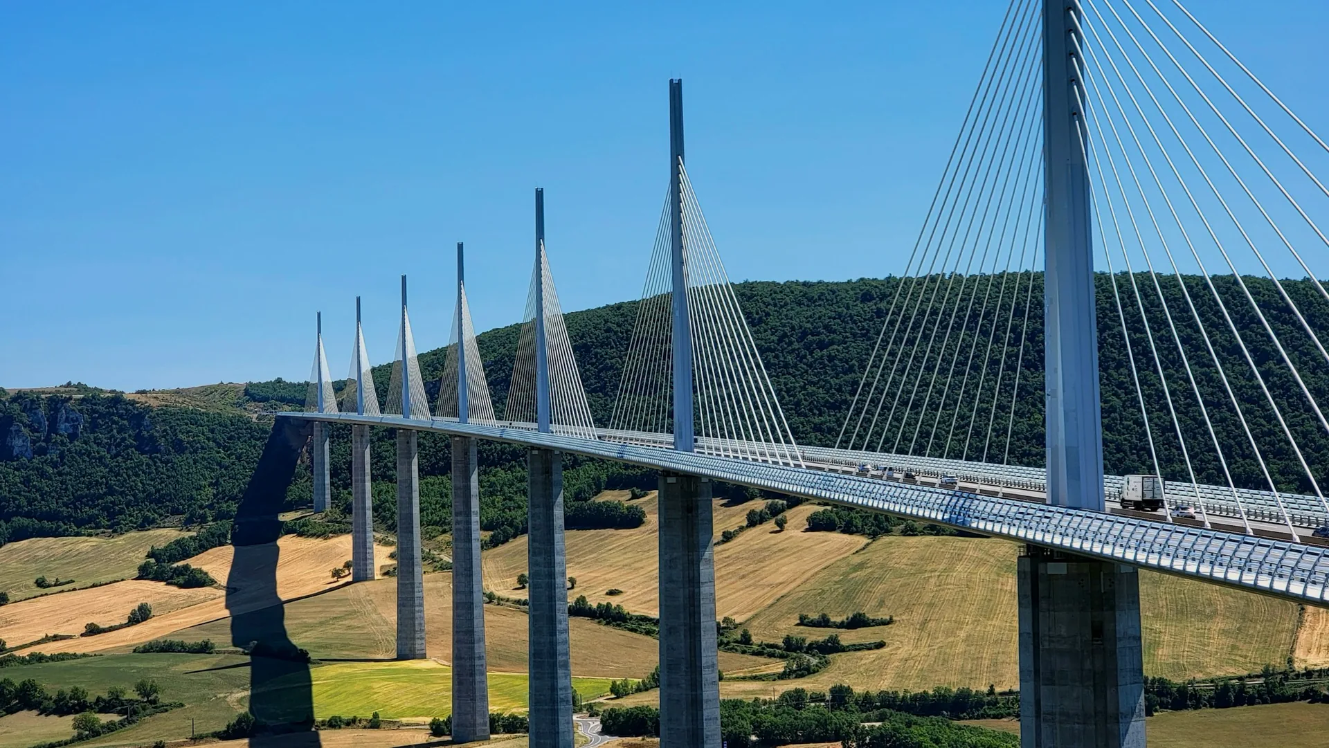 A long cable-stayed road bridge spanning a broad green valley.