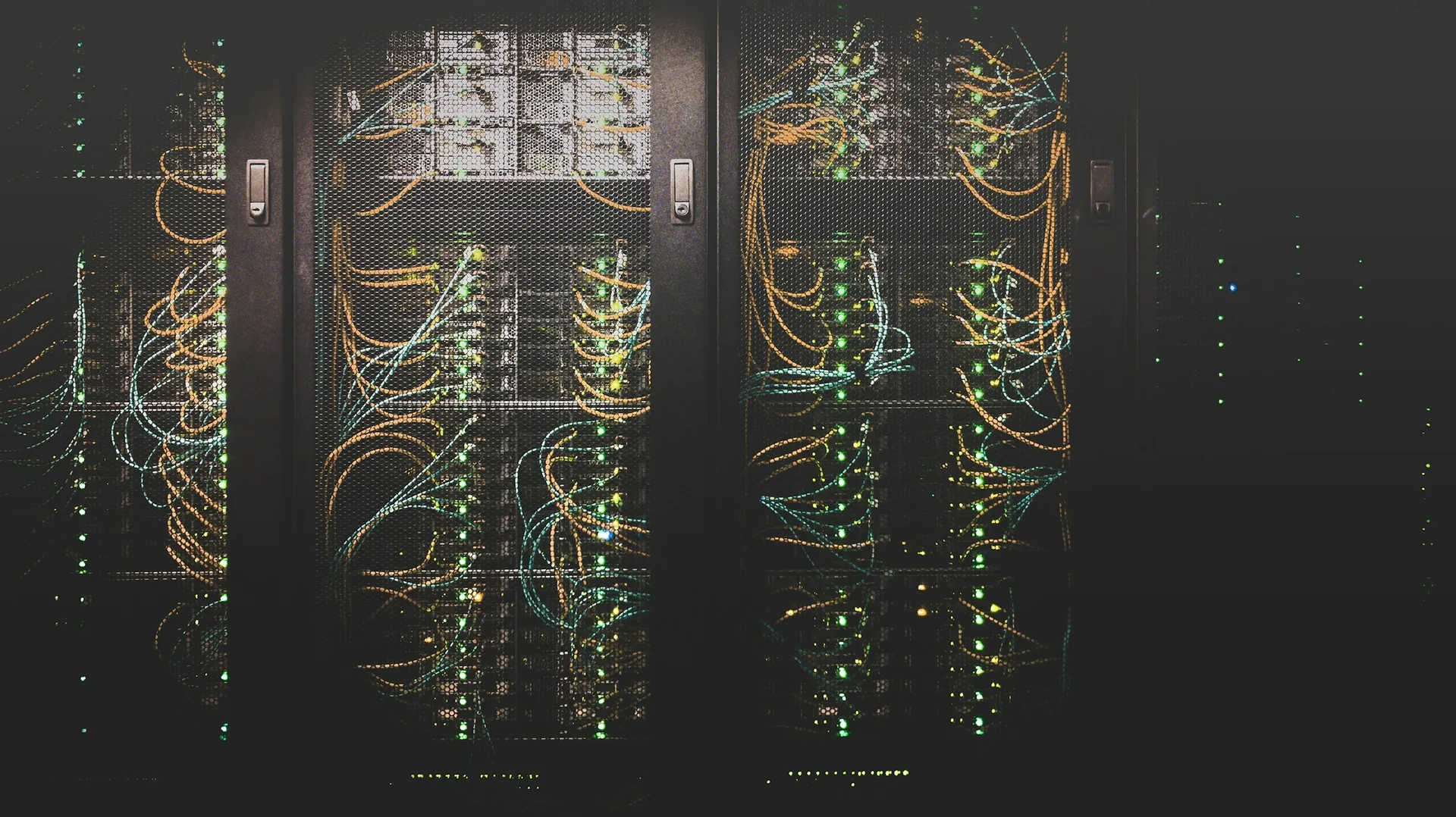 Server racks with illuminated status lights and network cables behind black mesh doors.